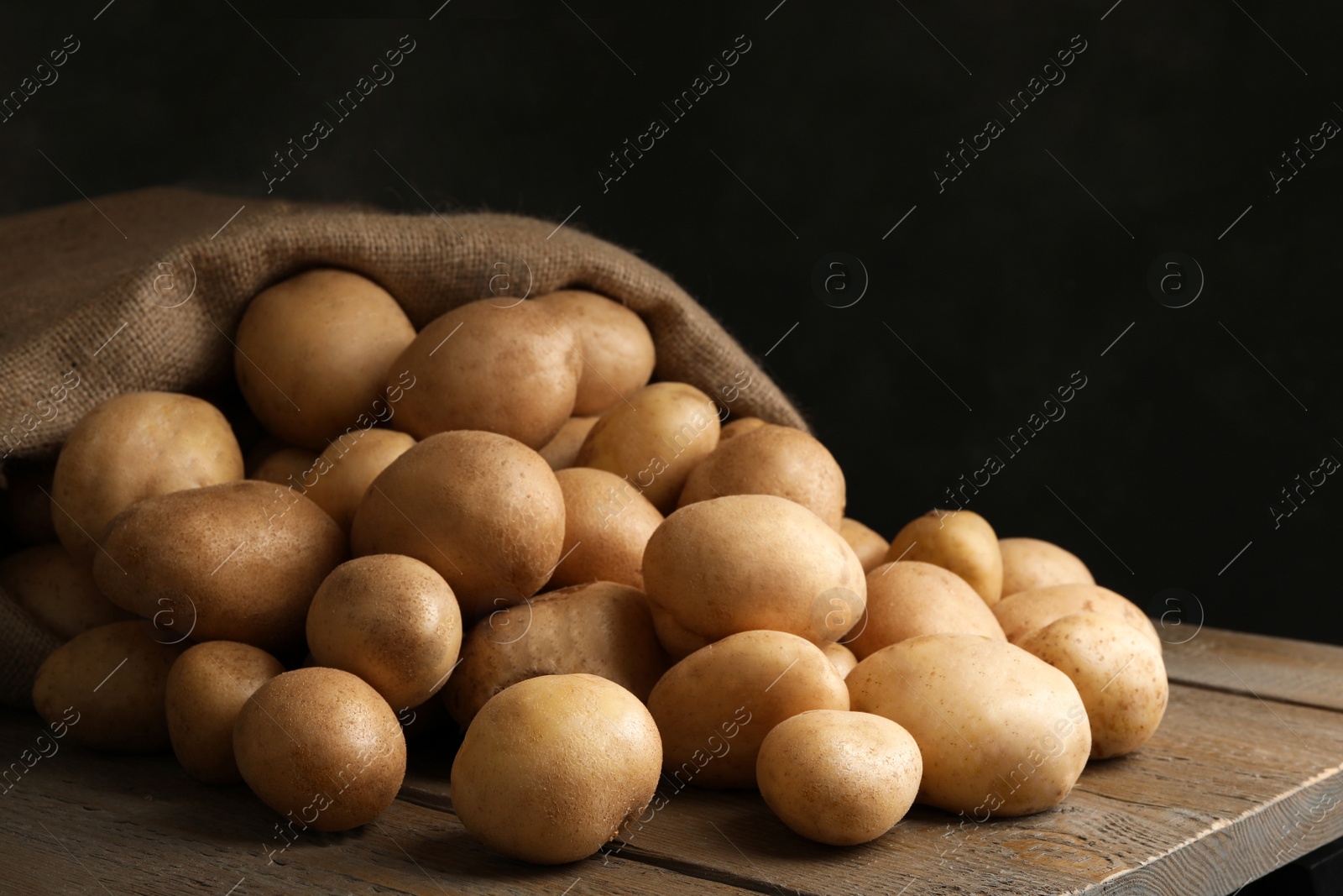 Photo of Raw fresh organic potatoes on wooden table against dark background