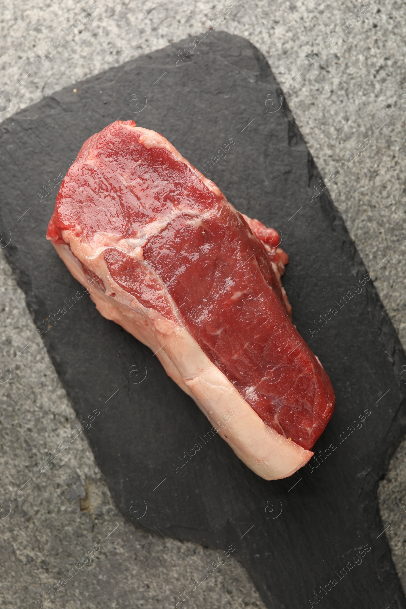 Photo of Piece of raw beef meat on grey textured table, top view