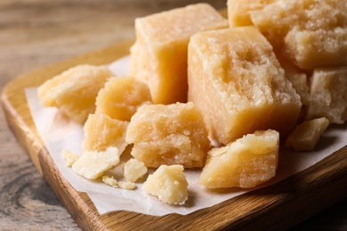 Photo of Pieces of delicious parmesan cheese on wooden board, closeup