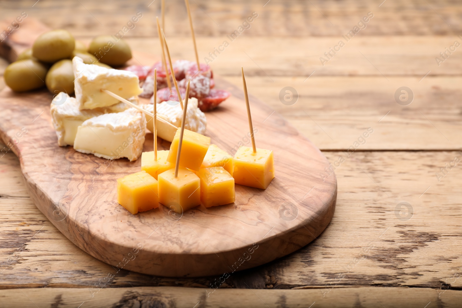 Photo of Toothpick appetizers. Pieces of different cheese on wooden table, closeup view with space for text