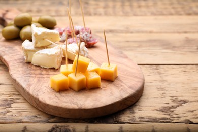 Toothpick appetizers. Pieces of different cheese on wooden table, closeup view with space for text