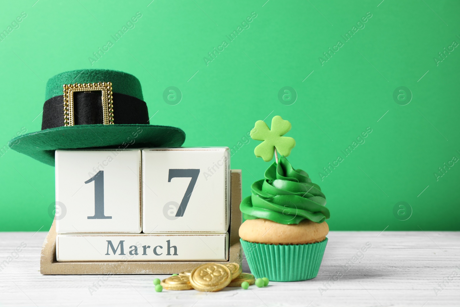 Photo of Decorated cupcake, wooden block calendar, hat and coins on white table. St. Patrick's Day celebration