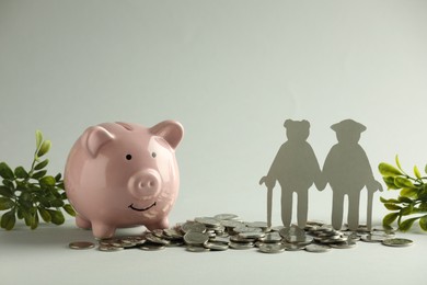 Pension savings. Figure of senior couple, piggy bank, coins and green twigs on grey background