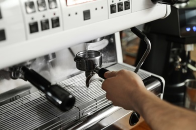 Photo of Barista cleaning portafilter at coffee machine in cafe, closeup