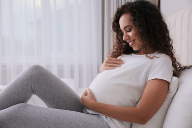 Photo of Pregnant young African-American woman sitting on bed at home