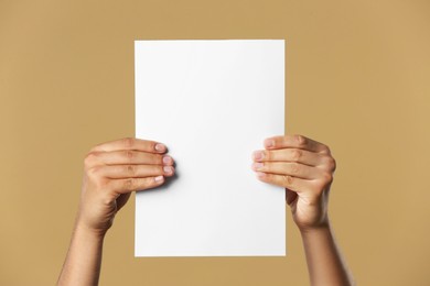 Man holding sheet of paper on beige background, closeup. Mockup for design