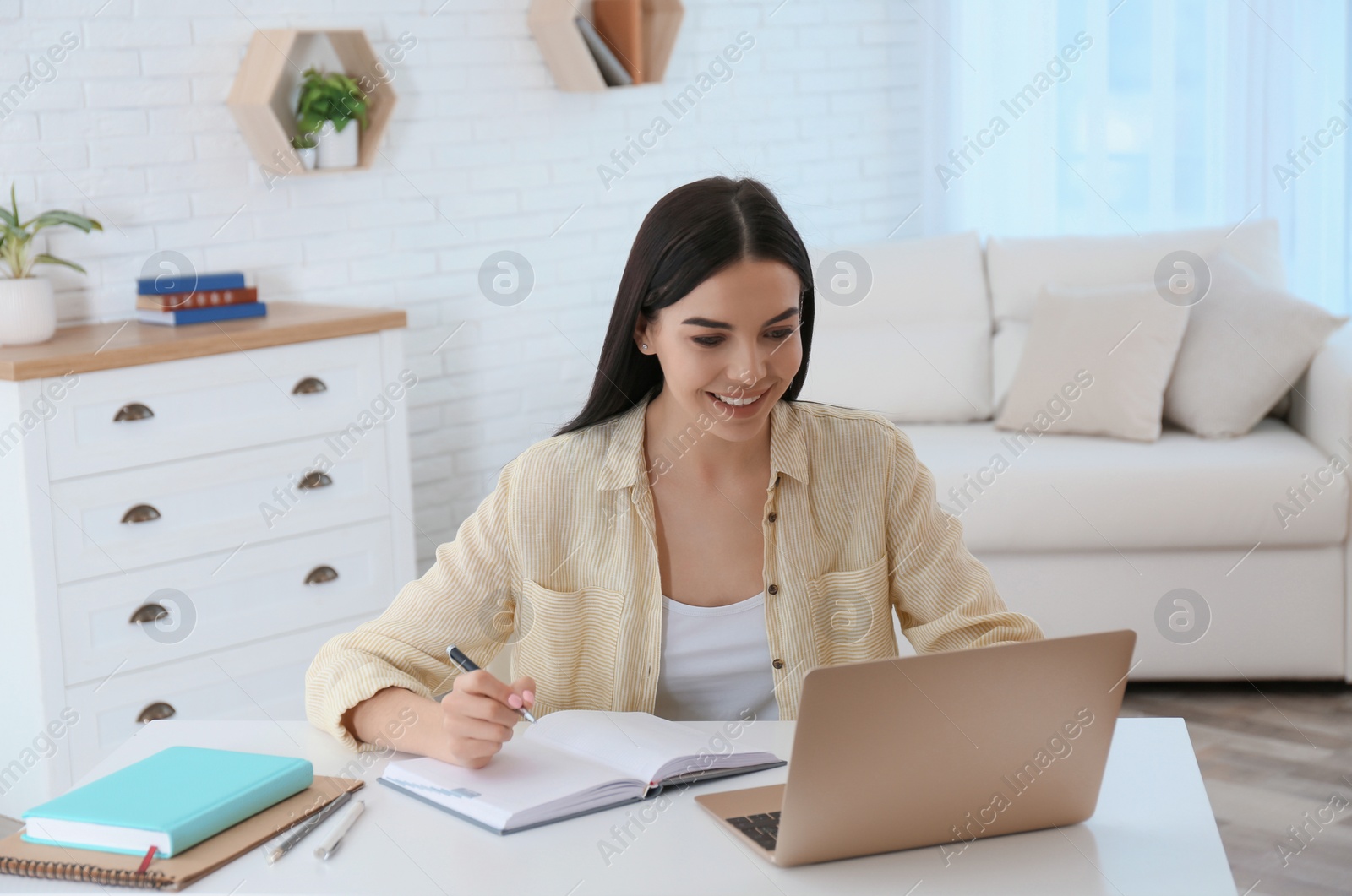 Photo of Young woman taking notes during online webinar at table indoors