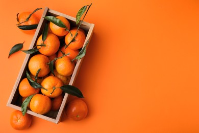 Photo of Wooden crate with fresh ripe tangerines and leaves on orange table, flat lay. Space for text