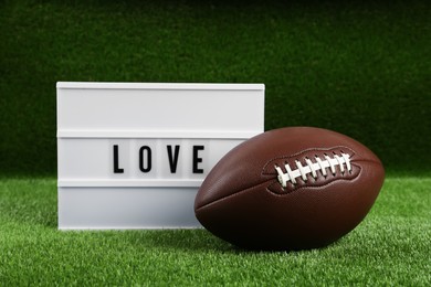 Photo of American football ball and lightbox with word Love on green grass