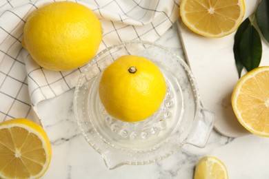 Photo of Glass squeezer and fresh lemons on white marble table, flat lay