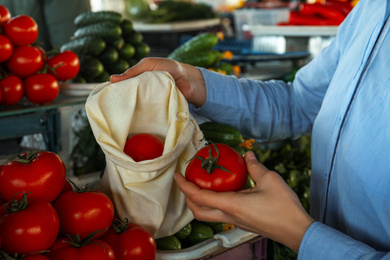 Photo of Woman putting tomato into cotton eco bag at wholesale market, closeup. Life without plastic