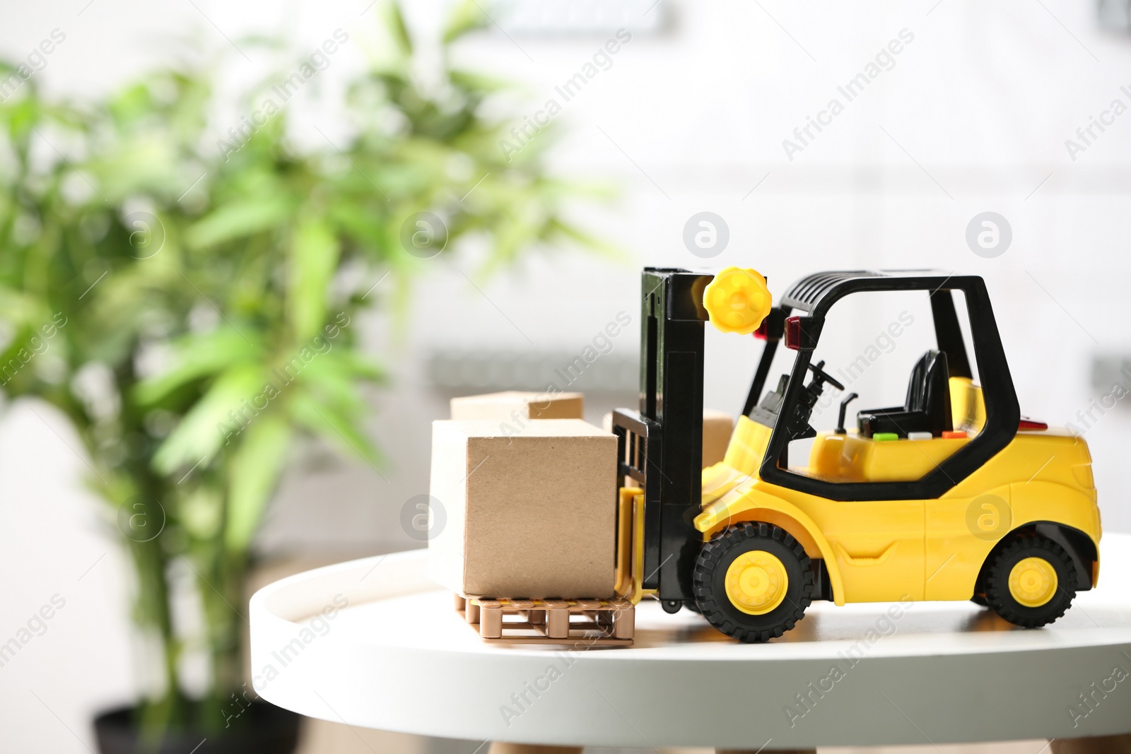 Photo of Toy forklift with cardboard box on table against blurred background. Courier service