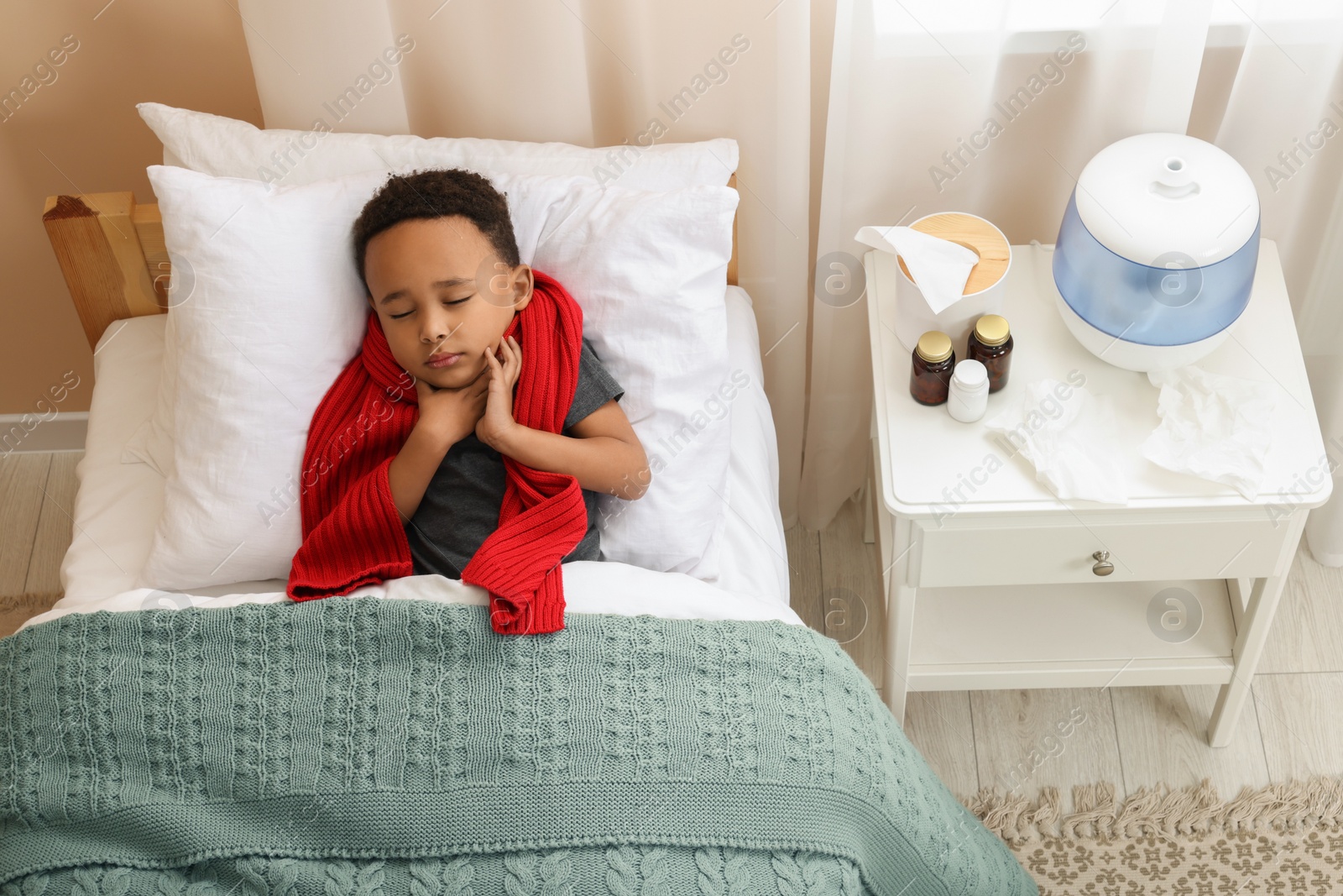 Photo of African-American boy with scarf lying in bed indoors, above view. Cold symptoms