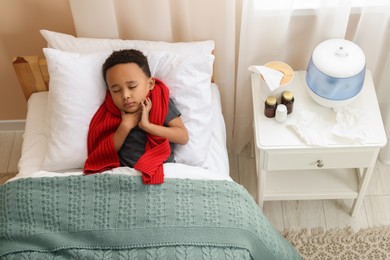 Photo of African-American boy with scarf lying in bed indoors, above view. Cold symptoms