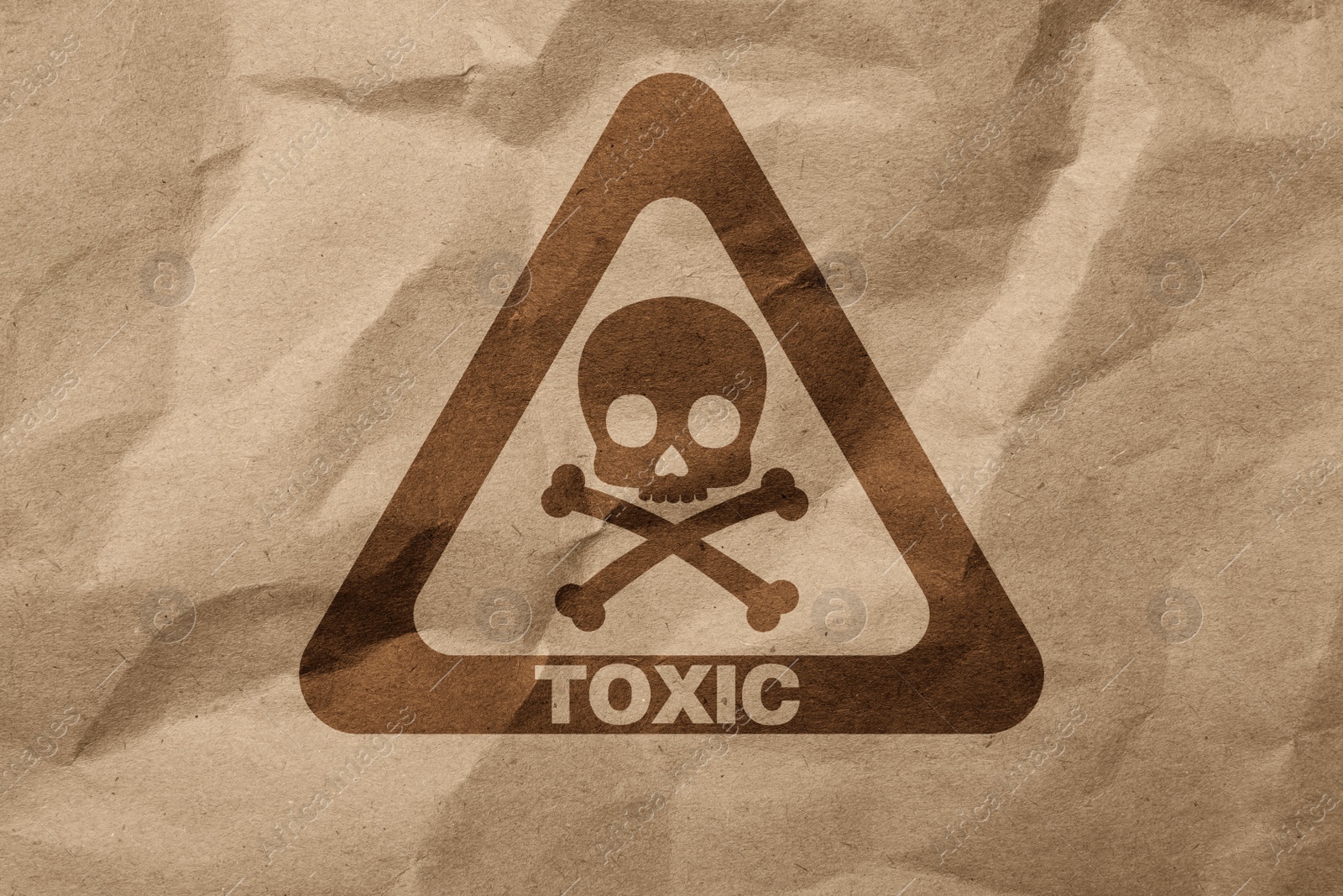 Image of Hazard warning sign (skull-and-crossbones symbol and word TOXIC) on crumpled kraft paper, top view