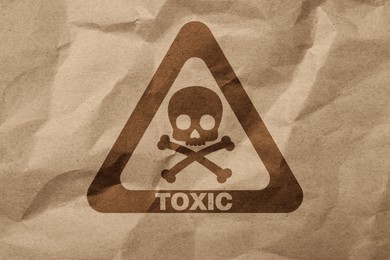 Hazard warning sign (skull-and-crossbones symbol and word TOXIC) on crumpled kraft paper, top view