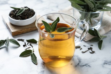 Photo of Cup of aromatic sage tea with fresh leaves on white marble table