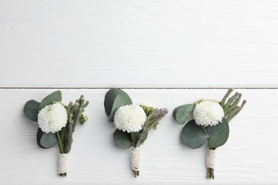 Small stylish boutonnieres on white wooden table, flat lay. Space for text