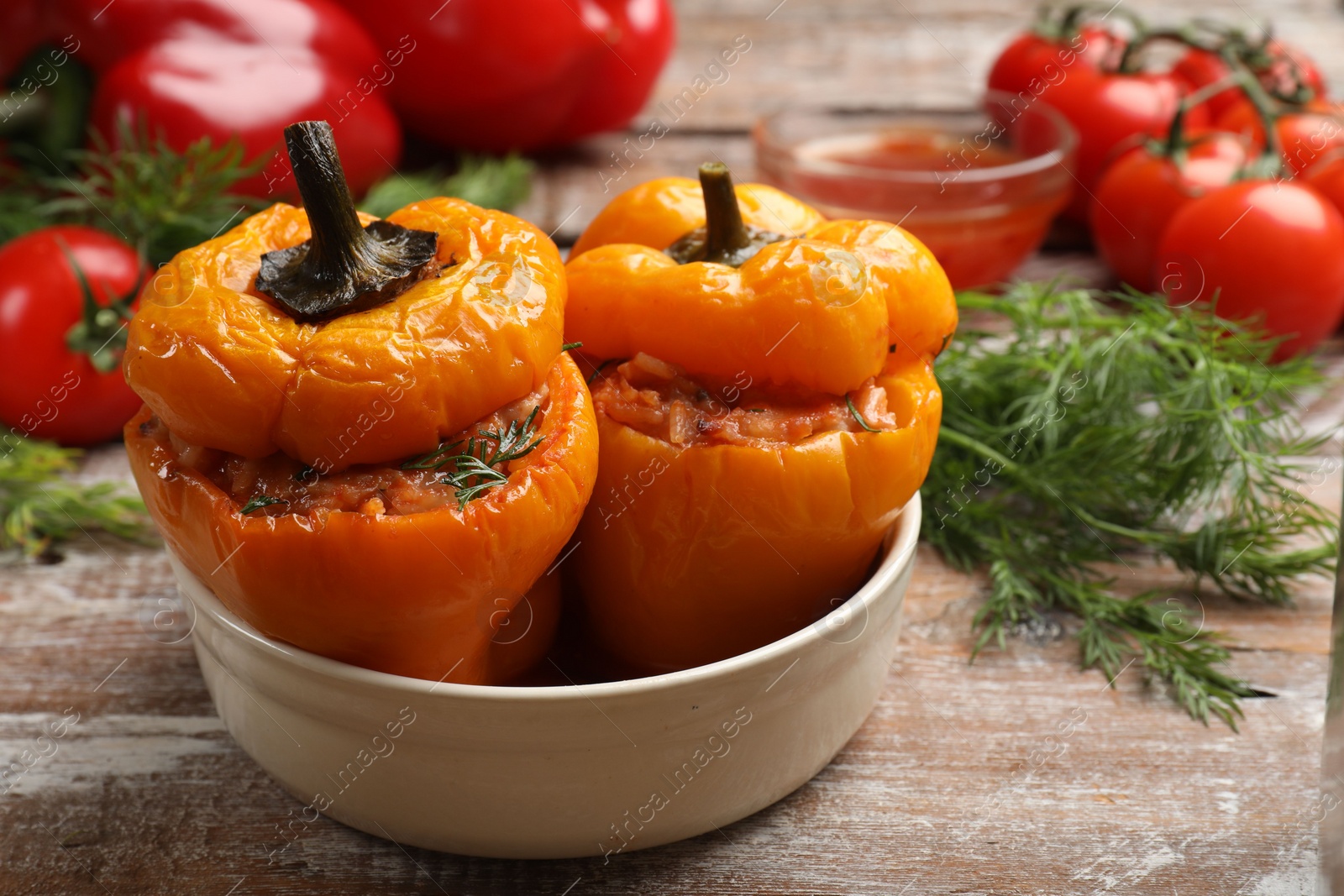 Photo of Tasty stuffed peppers in bowl on wooden table, closeup