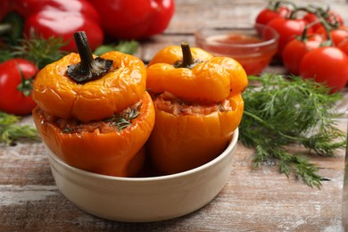 Photo of Tasty stuffed peppers in bowl on wooden table, closeup