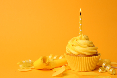 Delicious birthday cupcake with cream and burning candle on yellow background. Space for text