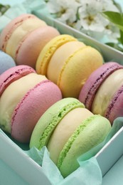 Photo of Many delicious colorful macarons in box on light blue background, closeup