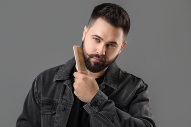 Photo of Handsome young man combing beard on grey background