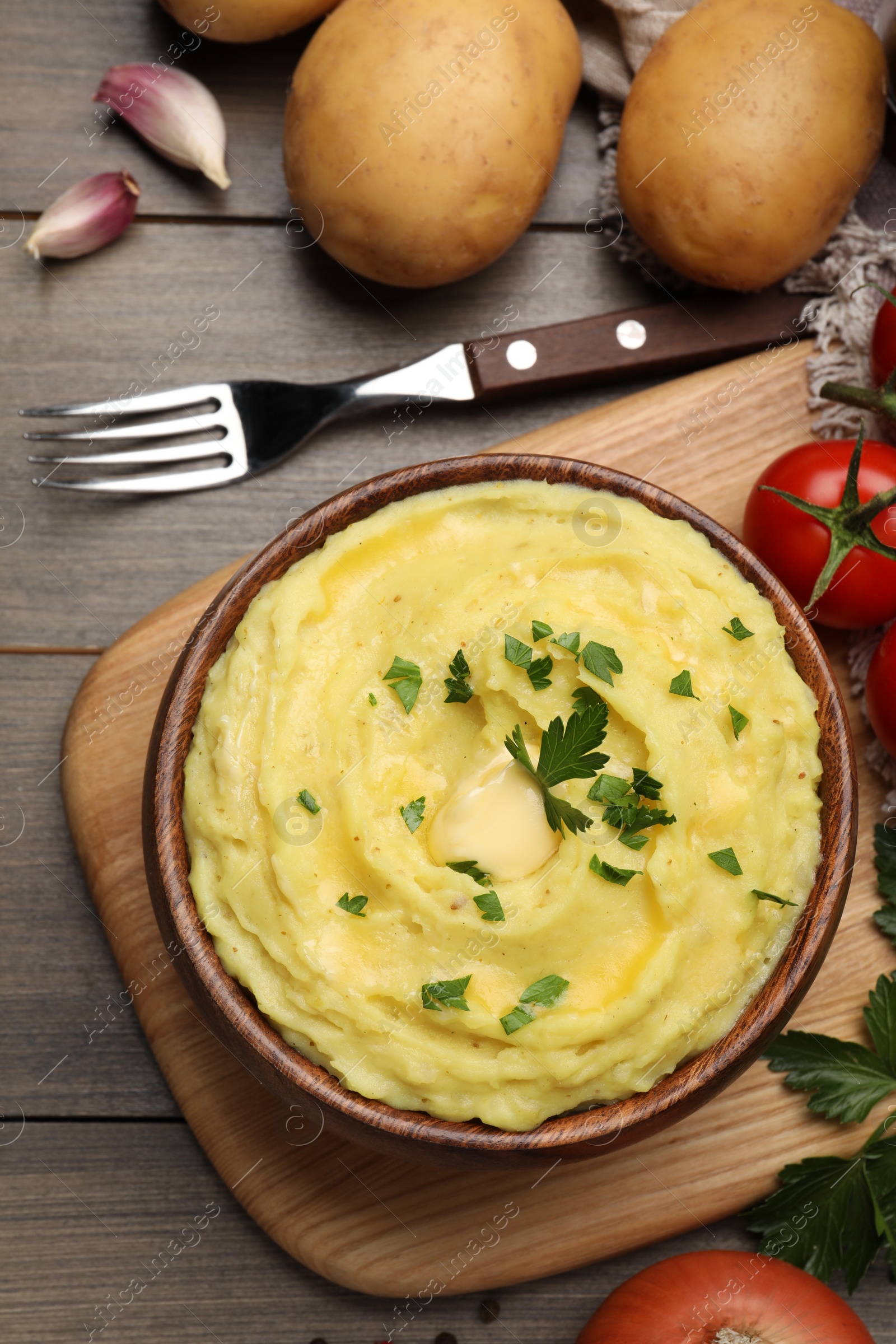 Photo of Bowl of freshly cooked mashed potatoes with parsley served on wooden table, flat lay