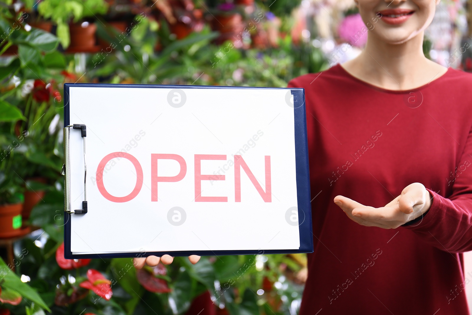 Photo of Female business owner holding OPEN sign in flower shop, closeup