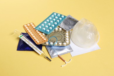 Photo of Contraceptive pills, condoms, intrauterine device and thermometer on yellow background. Different birth control methods