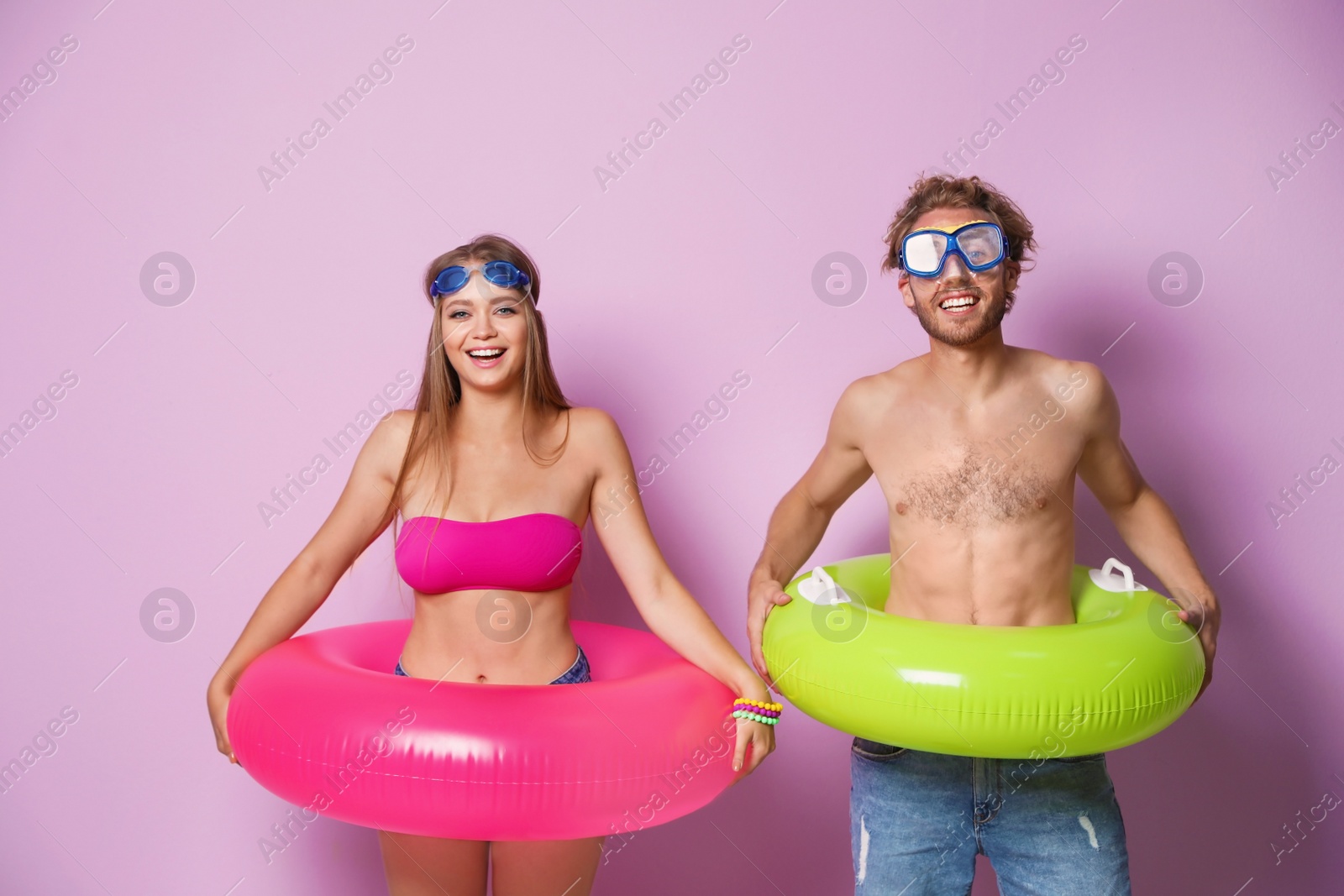 Photo of Young couple in beachwear and goggles with inflatable rings on color background