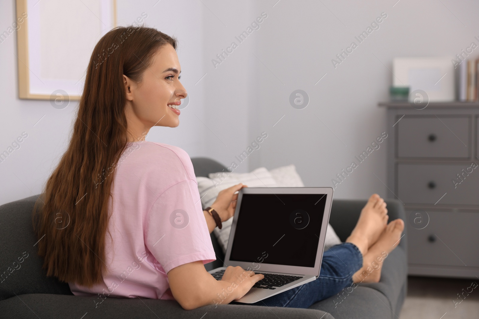 Photo of Happy young woman with laptop on sofa at home