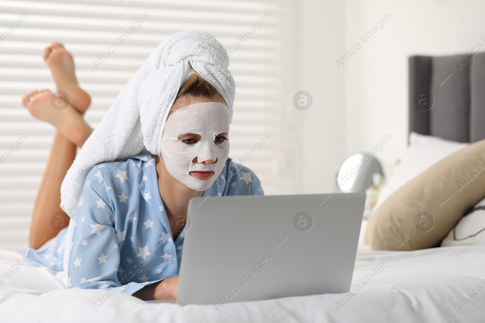 Photo of Young woman with face mask using laptop on bed at home. Spa treatments