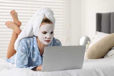 Young woman with face mask using laptop on bed at home. Spa treatments