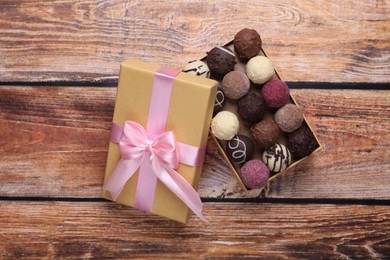 Photo of Open box with delicious chocolate candies on wooden table, top view