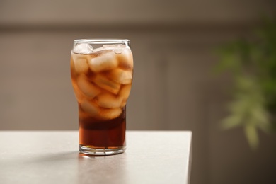 Photo of Glass of cola with ice on table against blurred background, space for text