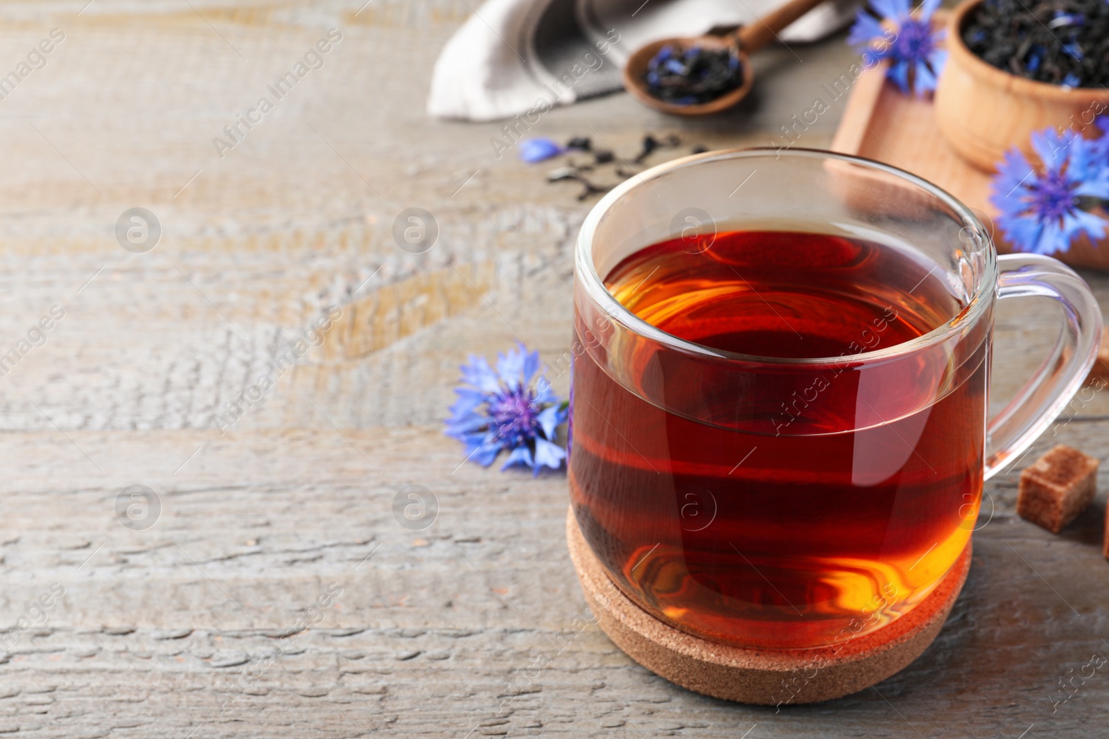 Photo of Glass cup of tea and cornflowers on wooden table, closeup. Space for text