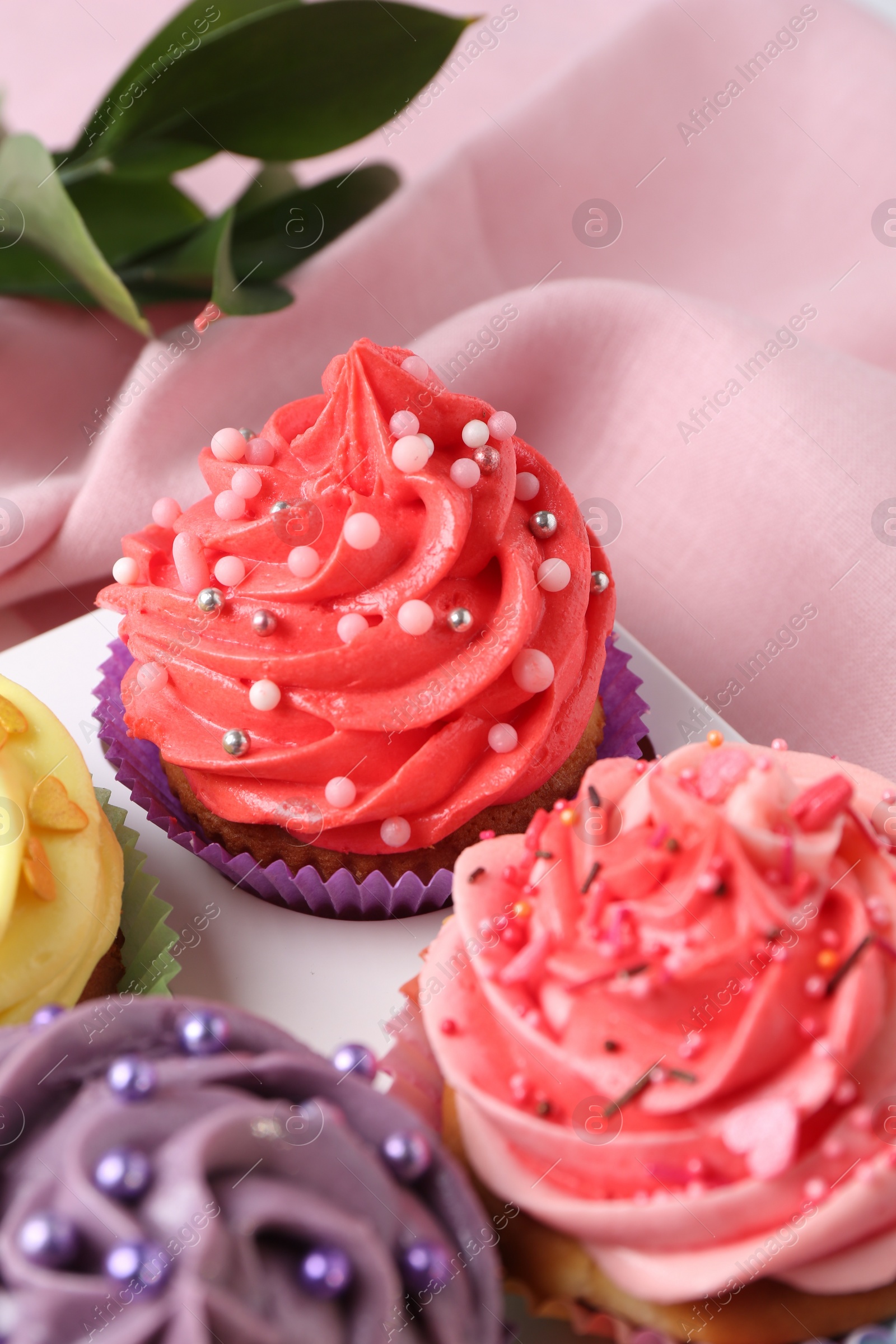 Photo of Delicious cupcake with bright cream on pink fabric, closeup