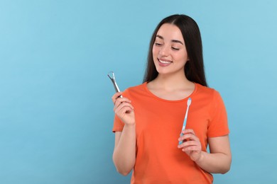 Happy woman with tongue cleaner and plastic toothbrush on light blue background, space for text