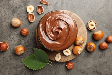 Photo of Tasty chocolate hazelnut spread and nuts on grey table, flat lay