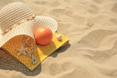 Photo of Straw hat, towel and orange on sand. Space for text