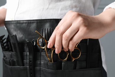 Photo of Hairstylist with professional tools in waist pouch on grey background, closeup