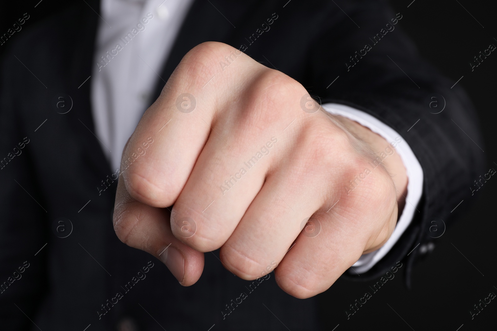 Photo of Businessman showing fist with space for tattoo on black background, closeup