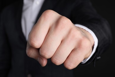 Photo of Businessman showing fist with space for tattoo on black background, closeup