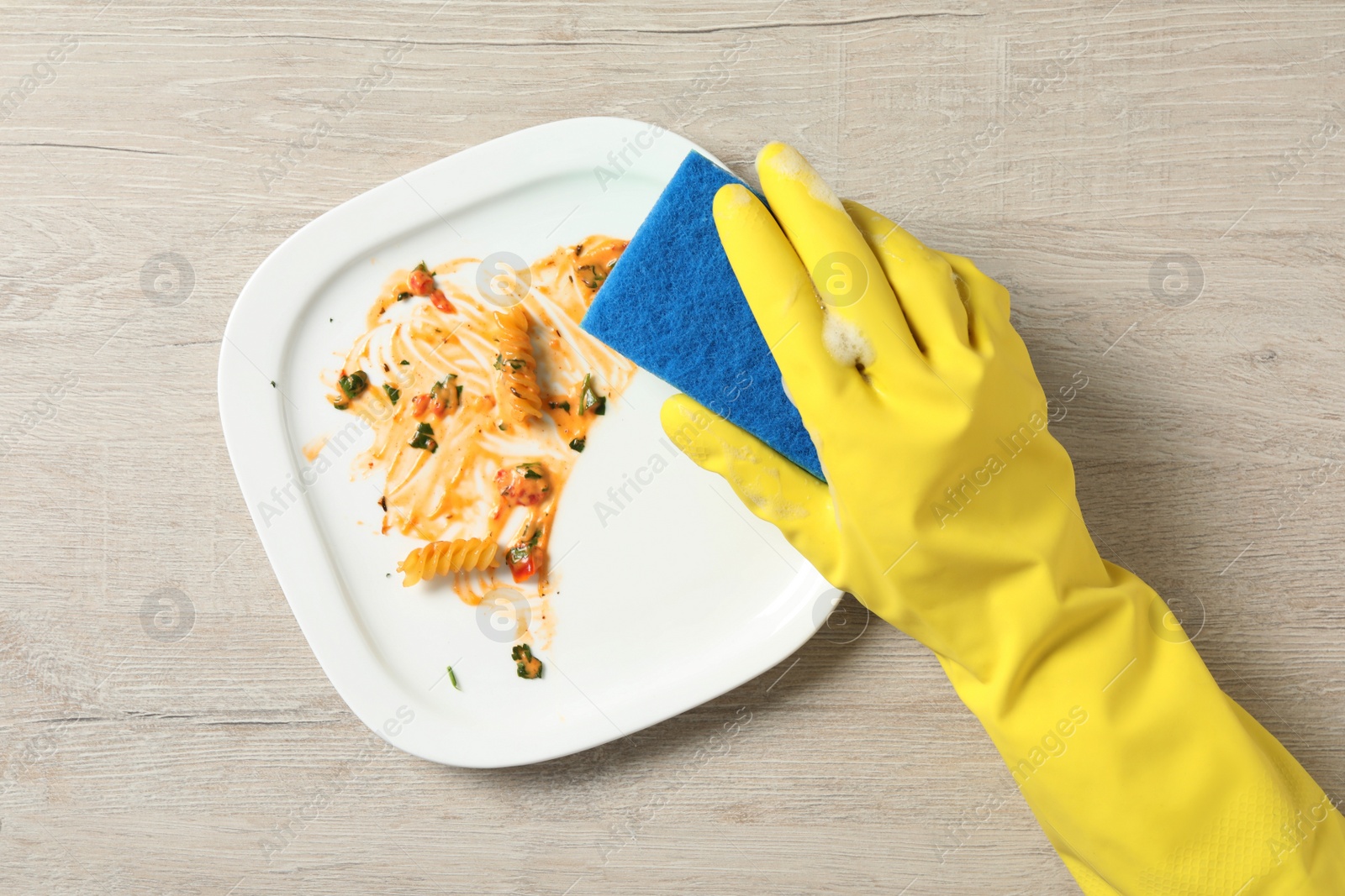 Photo of Woman washing dirty plate at light wooden table, top view