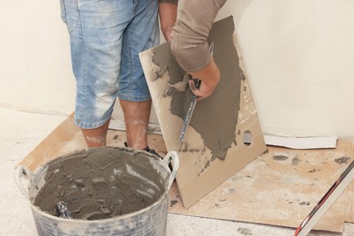 Photo of Worker spreading adhesive mix over tile with spatula, closeup