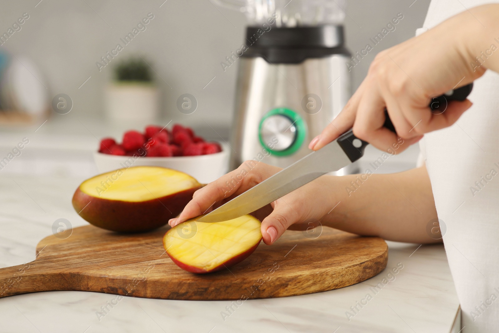 Photo of Woman preparing mango for tasty smoothie at white marble table in kitchen, closeup