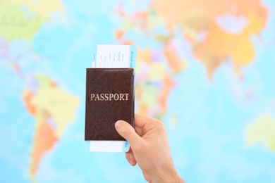 Photo of Man holding passport with ticket against blurred map in travel agency, closeup