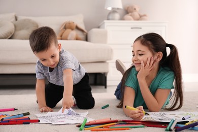 Photo of Cute children coloring drawings on floor at home