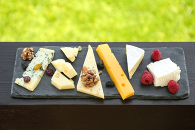 Photo of Different types of delicious cheeses and snacks on wooden railing outdoors, above view